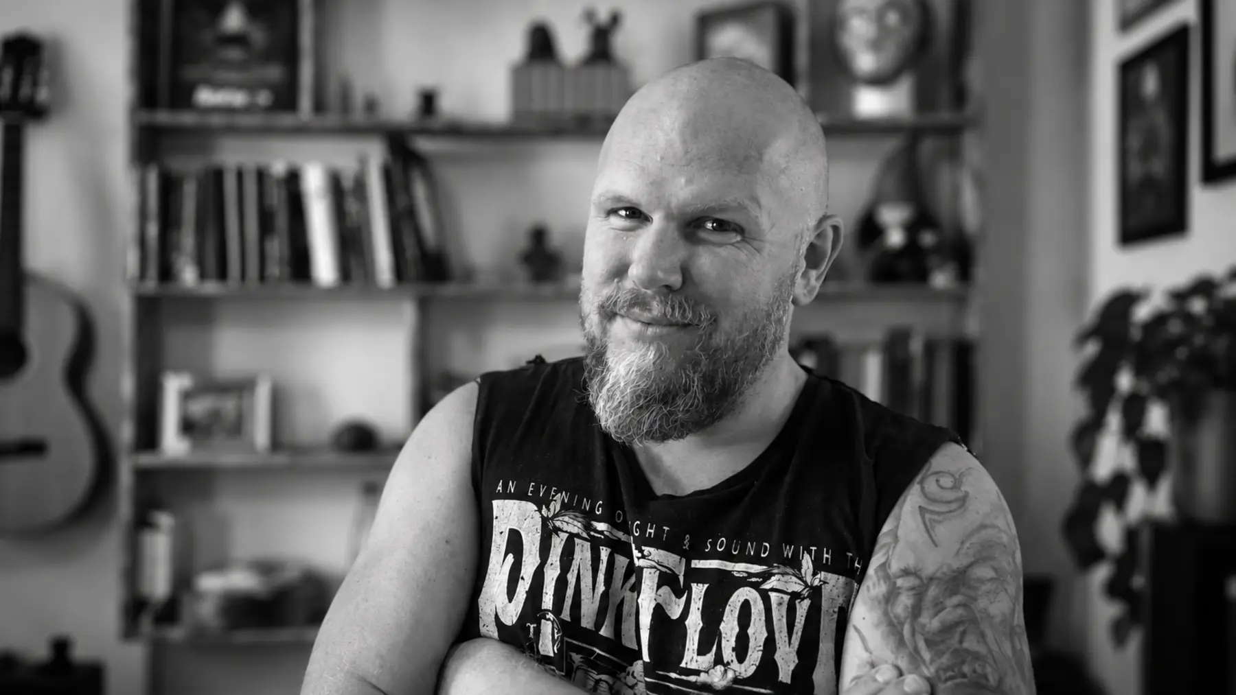 Jan Abraham, Porträt in Schwarzweiß, vor einem Bücherregal mit Gitarre